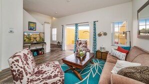 A spacious living room with a large sofa, a coffee table, and a patterned rug. There is a television mounted on the wall, a window with curtains, and a door leading to another room. - Newly Renovated, Spacious 3bd/2.5ba Villa With Lake View, Near Disney #3tv709 (Kissimmee)
