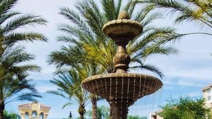 A multi-tiered fountain with water cascading down, surrounded by palm trees and a building with a decorative facade in the background. - Roomy and Modern 3bd/2ba Home With Balcony #3vc201 (Orlando)