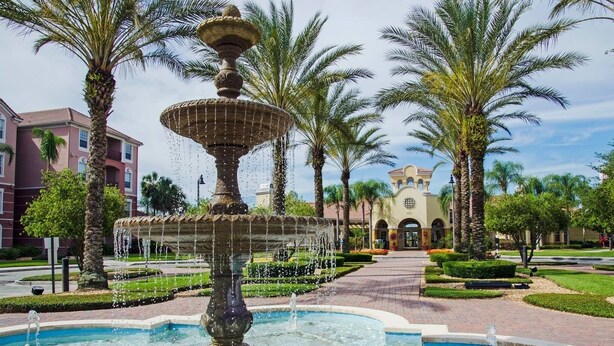 A fountain with multiple tiers and water jets, surrounded by palm trees and a building with a tiled roof in the background. - Roomy and Modern 3bd/2ba Home With Balcony #3vc201 (Orlando)