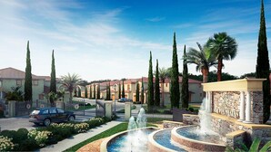 A gated residential area with a fountain, palm trees, and houses with red-tiled roofs.