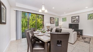 A modern living room with a dining area, large windows, and a flat-screen TV.