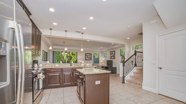 A spacious kitchen with dark wood cabinets, a granite countertop, and a stainless steel refrigerator.