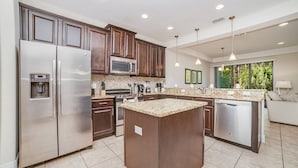 A modern kitchen with stainless steel appliances, a granite countertop island, and a view of greenery outside.
