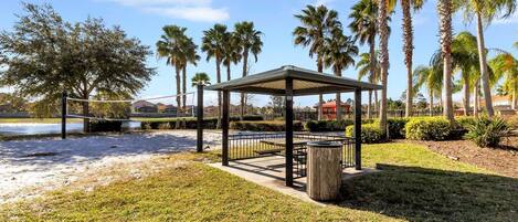 A gazebo with a metal railing, surrounded by palm trees and a grassy area.