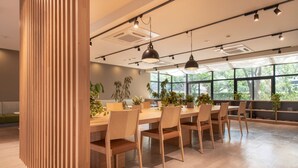 A modern meeting room with a long table, chairs, pendant lights, and potted plants. - Rupo Kenchoguchi Cozy Hotel (Fukuoka)