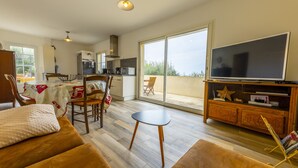 Amplia sala de estar con sofá, una mesita, televisor y un balcón con vistas.