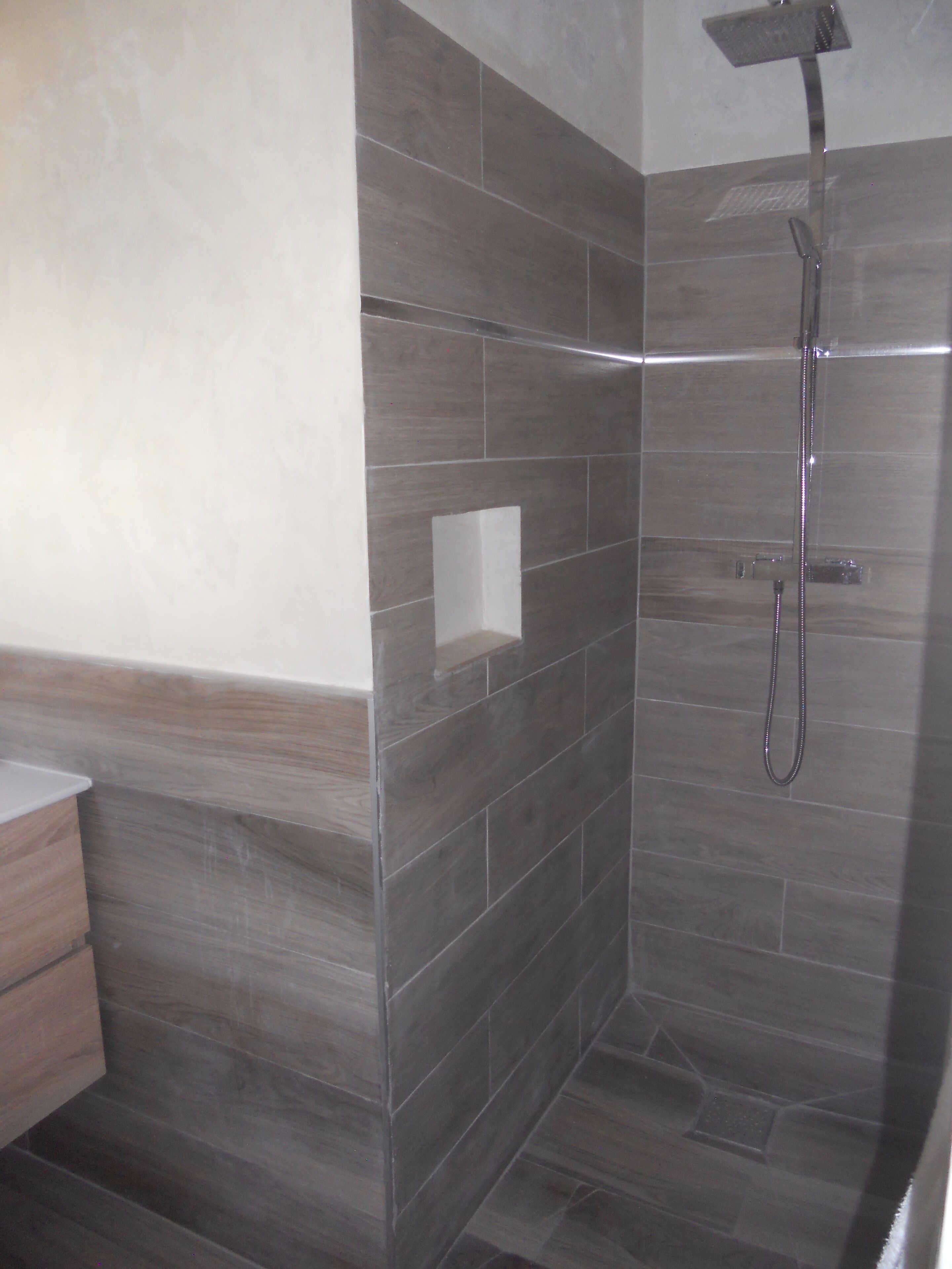 A shower area with a glass door, a handheld showerhead, and a wall-mounted control panel.