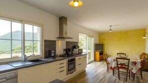 Una cocina moderna con una isla grande, horno empotrado, microondas y cafetera. Hay un comedor con mesa y sillas, y un televisor sobre un mueble.