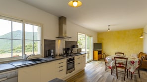 Una cocina moderna con una isla grande, horno empotrado, microondas y cafetera. Hay un comedor con mesa y sillas, y un televisor sobre un mueble.