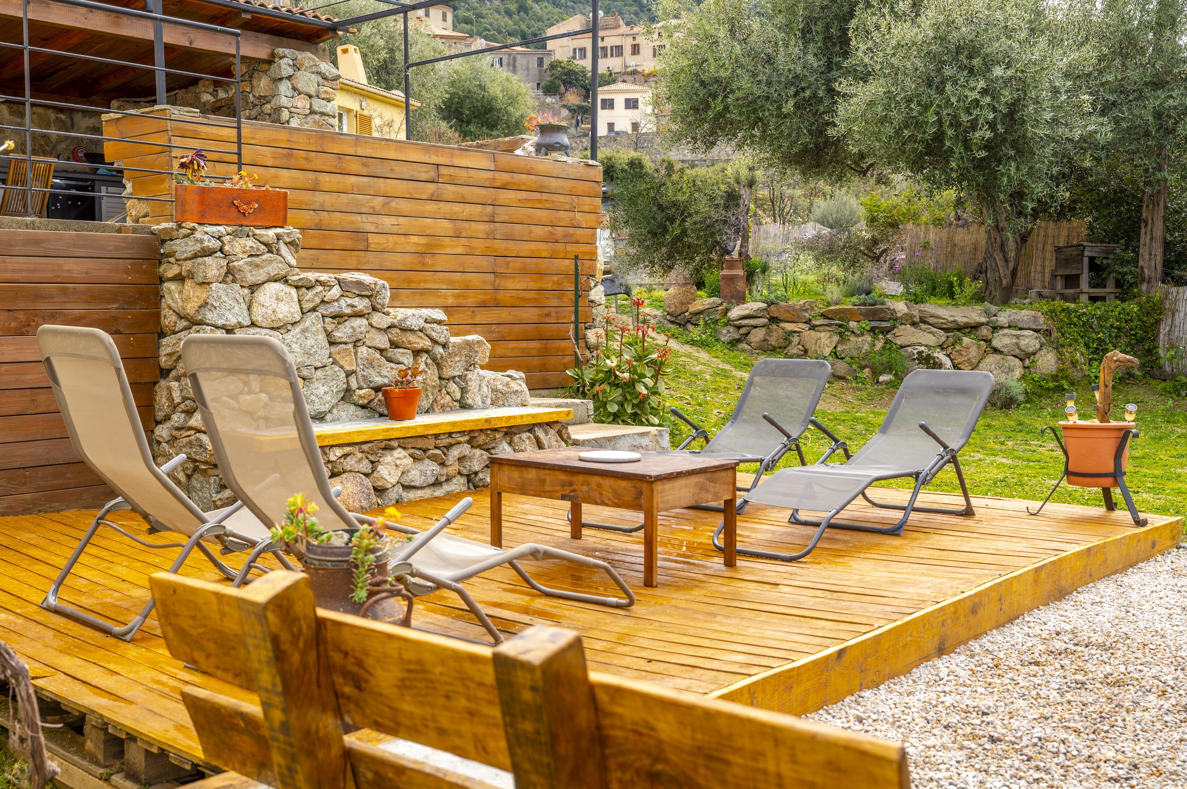 An outdoor patio with wooden furniture, stone walls, and a view of the surrounding landscape.
