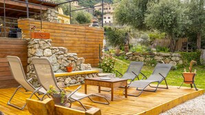 Un patio al aire libre con mobiliario de madera, paredes de piedra y vistas del paisaje circundante.