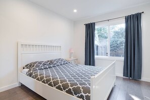 Une chambre à coucher avec un lit, une table de chevet, une fenêtre avec des rideaux et une vue sur les arbres à l’extérieur.