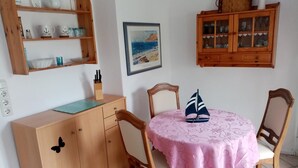 A dining area with a wooden cabinet, a table with a pink tablecloth, and a sailboat decoration.