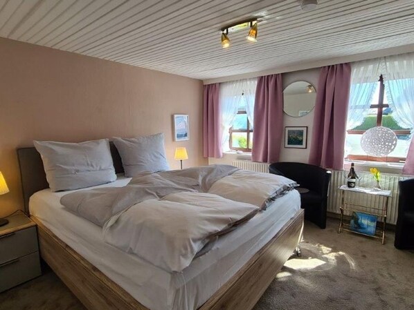 Un dormitorio con una cama grande, mesitas de noche, un escritorio con silla, una ventana con cortinas y un radiador.