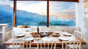 Une table à manger dressée pour six personnes, avec des chaises blanches, une vue sur la mer et une pergola en bois au-dessus.