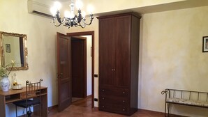 A bedroom with a bed, a wooden wardrobe, a desk with a chair, a mirror, and a chandelier. - Le Querce (Formello)