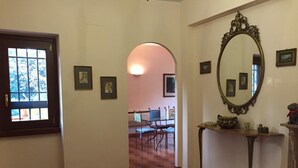 A hallway with a patterned rug, a door with a window, framed pictures on the walls, a mirror, and a table with decorative items. - Le Querce (Formello)