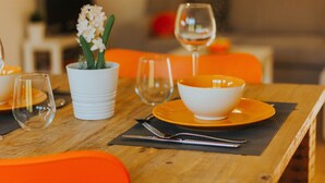 Une table à manger dressée avec un saladier blanc, des assiettes orange, un verre à vin et une plante en pot.