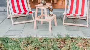 Un espace patio avec deux chaises de plage à rayures, une petite table avec une bouteille et un ensemble de salle à manger avec des chaises orange.