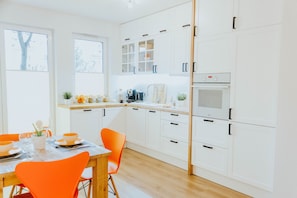 A modern kitchen with white cabinetry, a wooden countertop, and a dining area with orange chairs. - Wektor Idea Apartment Gdańsk (Gdansk)