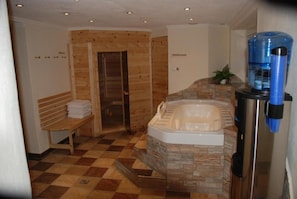 A bathroom with a stone wall, a bench, a shower, and a water dispenser.