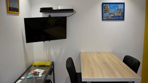 Ein Konferenzraum mit einem an der Wand montierten Flachbildfernseher, einem Holztisch und schwarzen Stühlen.