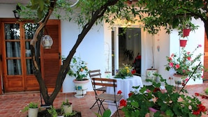 A patio with a wooden table and chairs, surrounded by potted plants and flowers. - Vaya Zorba Studios (Skiathos)