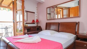A hotel room with a wooden bed, a bedside table, a mirror, and a window with curtains. - Vaya Zorba Studios (Skiathos)