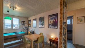A room with a pool table, green chairs, a wooden table, and framed posters on the wall. - Back to the 80'S Apartment (Saint-Egrève)