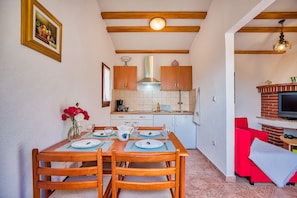 A dining area with a wooden table set for four, a kitchen with white cabinets and a red brick fireplace, and a red sofa in the living area.