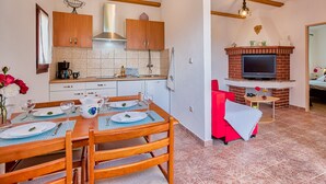 A kitchen with wooden cabinets, a stove, and a dining area with a table set for two. - Casa Oliveto - relax in Nature (Marčana)
