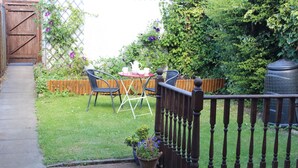 Een houten terras met een metalen hekwerk, een bloempot en een tafel met stoelen.