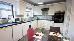 Een compacte keuken met witte kastjes, een magnetron, een vaatwasser en een dubbele oven.