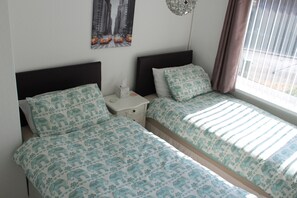 Une chambre double avec deux lits, une table de chevet, une lampe fixée au mur et une fenêtre avec des rideaux.