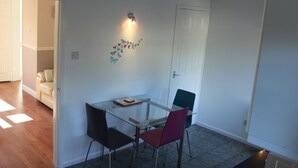 Een eetruimte met een glazen tafel, twee stoelen, een hanglamp en een decoratie aan de muur.