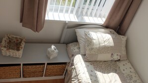 Een kleine, gezellige slaapkamer met een bed, een nachtkastje met een zakdoosje, een rieten mand en drie opbergmanden onder het bed.