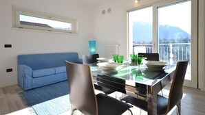 A modern dining area with a glass table, chairs, and a blue sofa. - Gardenia Apartment Ossuccio (Ossuccio)