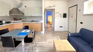 A modern kitchen with a dining area, a sofa, and a hallway leading to a bedroom. - Gardenia Apartment Ossuccio (Ossuccio)