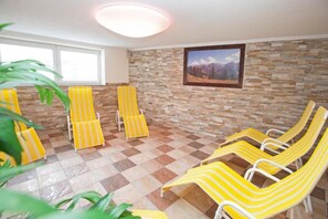 A room with a checkered floor, yellow-striped lounge chairs, a stone wall, and a framed picture.