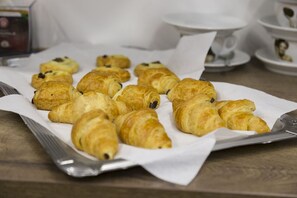 Una bandeja de croissants sobre una mesa, con una cafetera y tazas de té al fondo.