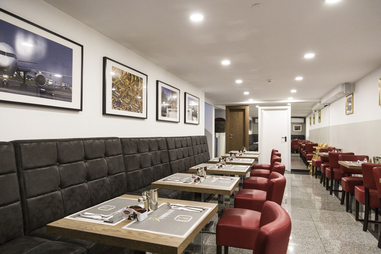 Ein Restaurant mit langen Tischen, roten Stühlen und einer schwarzen gepolsterten Bank, an den Wänden befinden sich gerahmte Bilder.