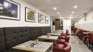 Un restaurant avec de longues tables et des chaises rouges, un banc noir rembourré et des tableaux encadrés accrochés au mur.