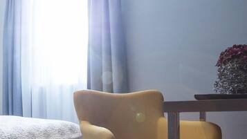 Ein modernes Hotelzimmer mit einem Bett, einem gelben Sessel, einem kleinen Tisch und einer Vase mit Blumen.