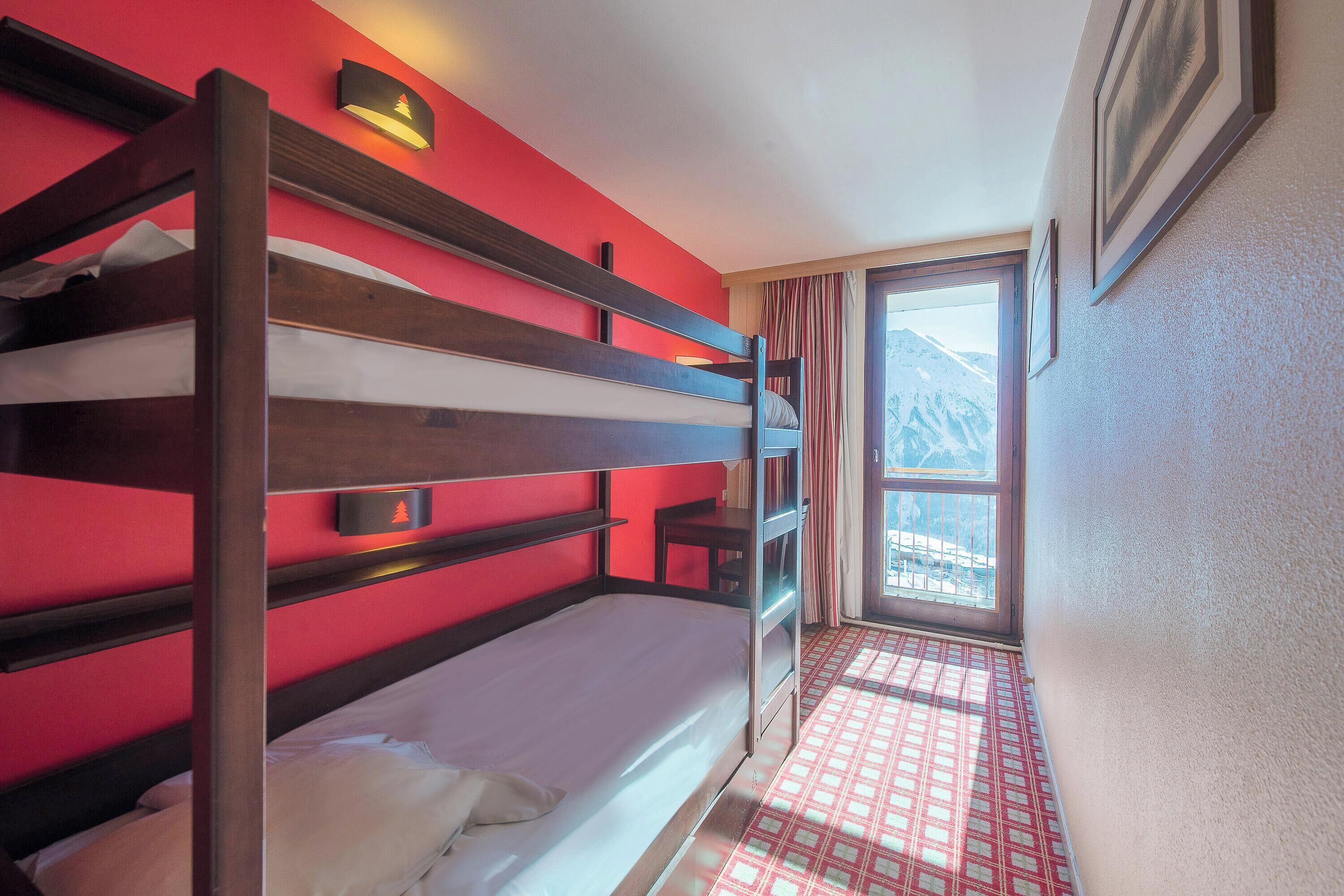 Habitación con literas, una pared roja, una ventana con vistas a la montaña y una alfombra estampada.