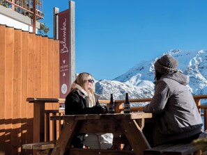 Two people sitting at a wooden table with bottles, overlooking a snowy mountain. - Belambra Clubs Orcières 1850 - Le Roc Blanc (Orcieres)