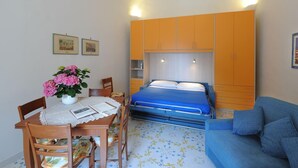 Une chambre à coucher de taille réduite, comprenant un lit, un canapé, une table à manger avec des chaises et un vase de fleurs.