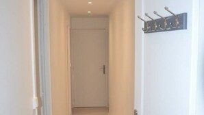 Un pasillo estrecho con suelo de madera, una puerta blanca a la derecha y un tablero de ganchos en la pared.