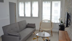Una sala de estar moderna con un sofá gris, un sillón de mimbre y una pequeña mesa blanca.