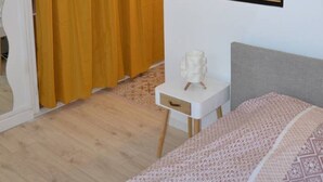 Un dormitorio con cama, mesita de noche, espejo y cortina amarilla.