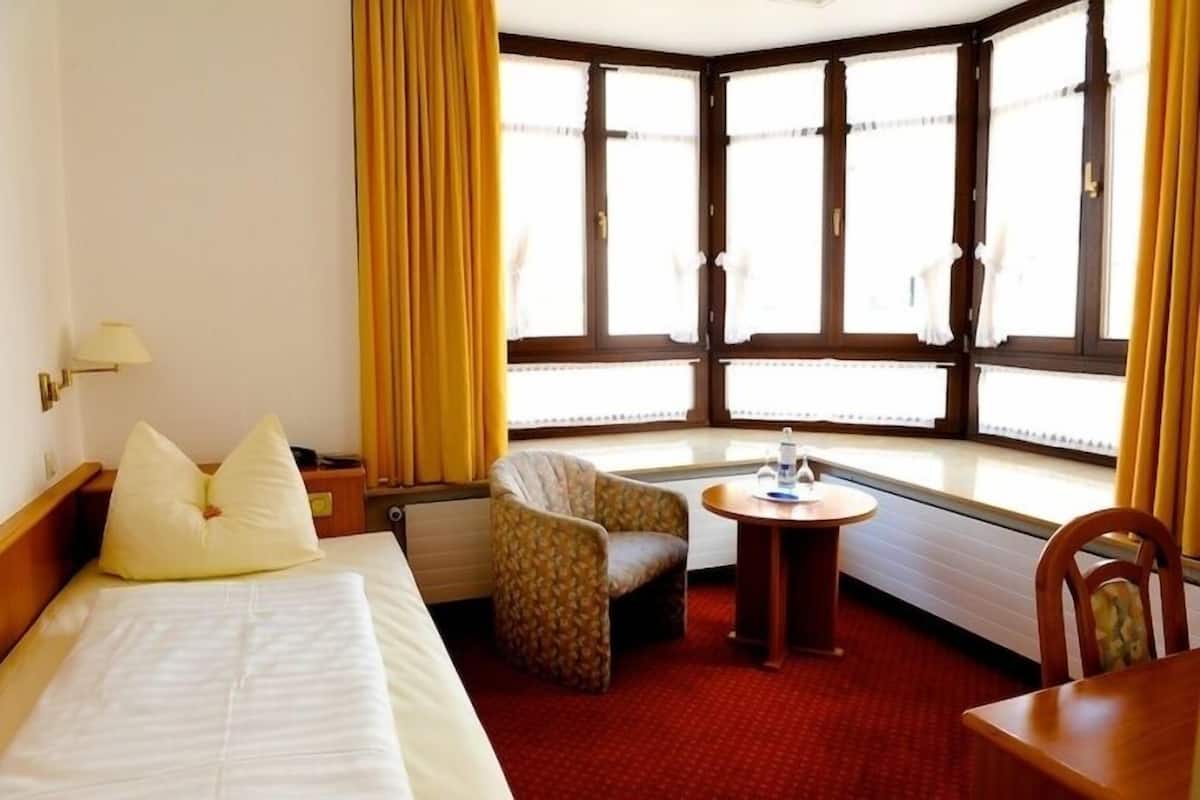 Una habitación de hotel con cama, una silla, una mesita y una ventana con cortinas.